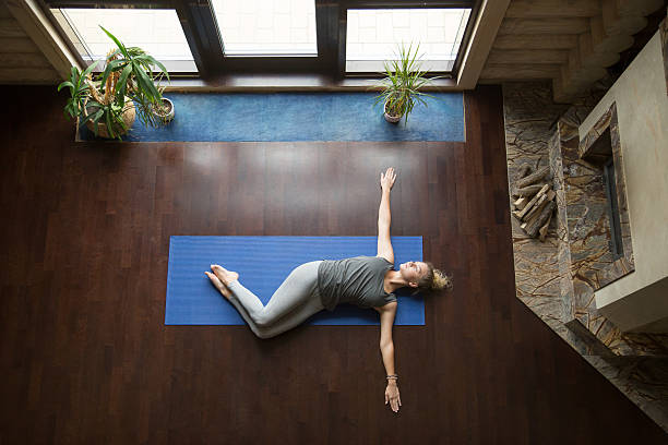 Yoga at home: Belly Twist Pose Attractive young woman working out in living room, doing yoga exercise on wooden floor, lying in Belly Twist Pose, Jathara Parivartanasana, resting after practice, full length, top view twisted stock pictures, royalty-free photos & images
