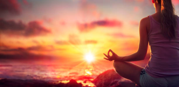 yoga ao pôr do sol - mulher na meditação - foco em primeiro plano e fundo desfocado - aperfeiçoamento pessoal - fotografias e filmes do acervo