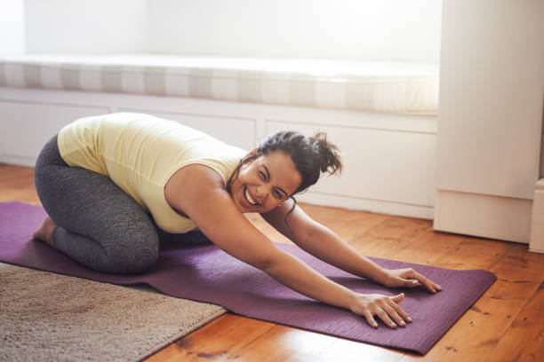 Yoga makes her really happy Shot of a beautiful young woman practicing yoga at home voluptuous women images stock pictures, royalty-free photos & images
