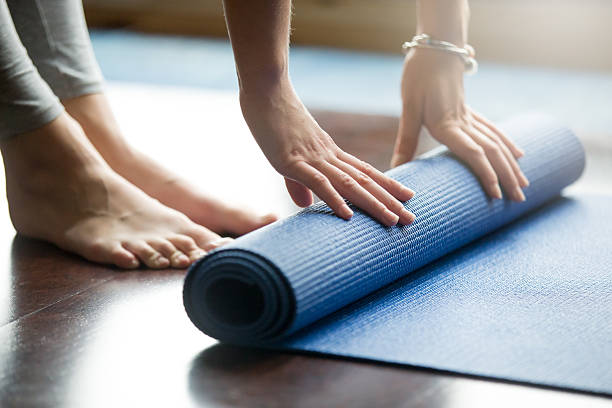 Yoga training concept Close-up of attractive young woman folding blue yoga or fitness mat after working out at home in living room. Healthy life, keep fit concepts. Horizontal shot barefoot photos stock pictures, royalty-free photos & images