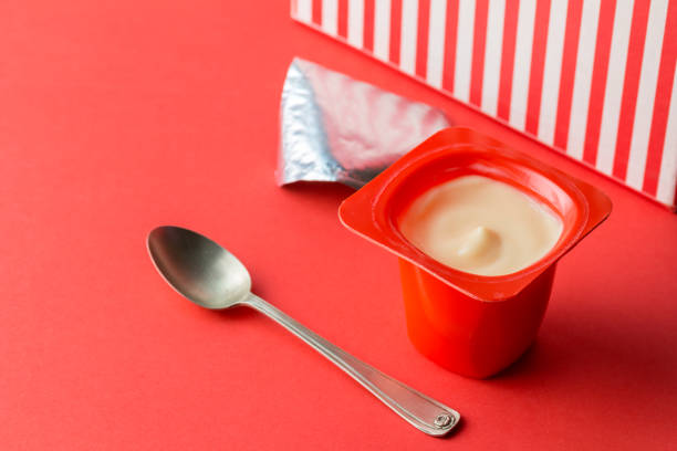 Yogurt cup on red background - single pot of fruit yoghurt in red plastic container, foil lid and small spoon with text space stock photo