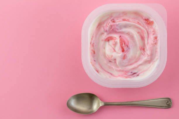 Yogurt cup with natural strawberry greek style yogurt swirled with real strawberries isolated on light pink background with small silver spoon stock photo