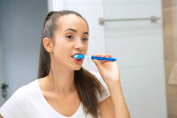 Yooung woman brushing her teeth at mirror stock photo
