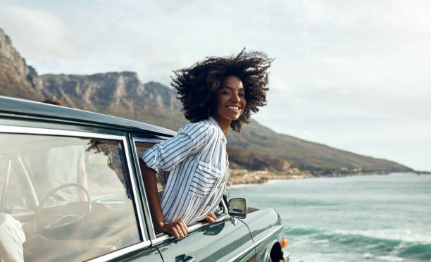 You don't need much to fill your heart with happiness Shot of a happy young woman leaning out of a car window on a road trip leaning stock pictures, royalty-free photos & images