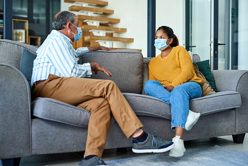 Shot of a senior father and daughter wearing medical masks while chatting on the sofa in his apartment