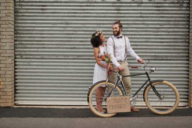 You had me at “I do” Shot of a newly married young couple taking their bicycle through the city on their wedding day newlywed stock pictures, royalty-free photos & images