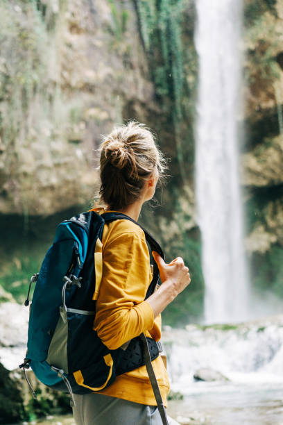 Young active unrecognizable woman from behind with a backpack looking at a waterfall in a canyon. stock photo