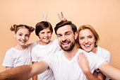 Young adorable attractive beautiful happy family laughing making selfie together. Boy and girl holding victory or peace sign behind their relatives' heads, mimicking bunny ears
