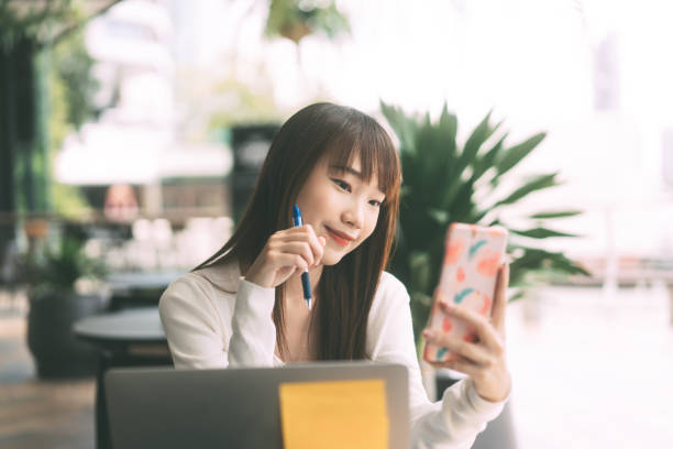 Young adult asian student woman using mobile phone for online application at indoor cafe. stock photo