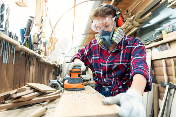 Young adult caucasian mid aged professional female carpenter grinding raw wood with orbital sander tool in carpentry diy workshop. Feminine women equality concept. Women do male hobby at workbench stock photo