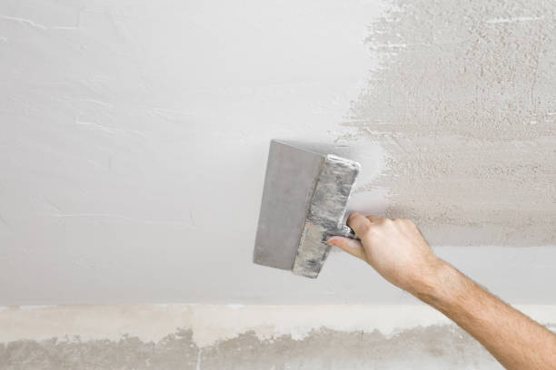 Young adult man hand using spatula and plastering ceiling with white fresh finishing putty. Closeup. Repair work of home. View from below. stock photo
