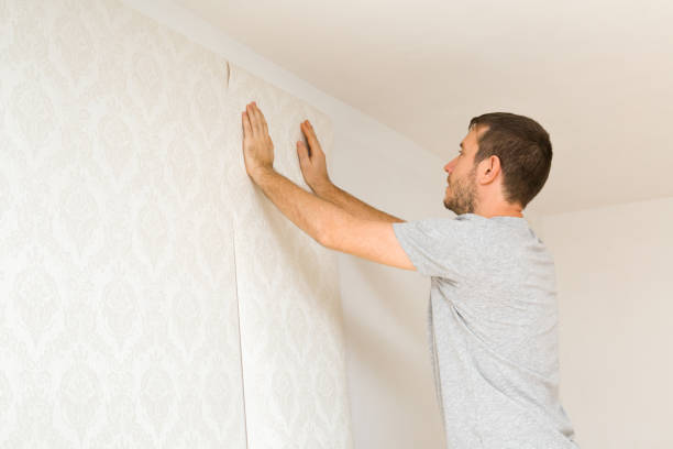Young adult man hands applying new wallpaper on white wall. Closeup. Repair work of home. Side view. stock photo