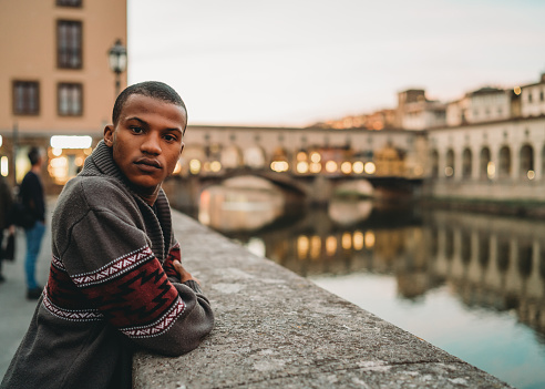 Young adult man portrait in the city during sunset against Arno River, Florence