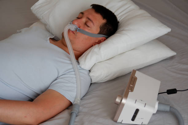 young adult man wearing under the nose nasal mask ( CPAP mask ) and using CPAP machine stock photo