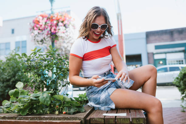 Young Adult Woman Doing Mobile Deposit With Smartphone A young adult women enjoys the summer sun in her town, depositing a check with her phone (remote deposit capture) to her bank. bank deposit slip stock pictures, royalty-free photos & images