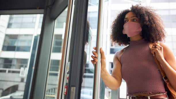 jonge volwassen vrouw die bureau ingaat dat gezichtsmasker draagt dat van camera kijkt - betreden stockfoto's en -beelden