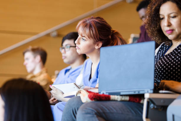 Young adult woman focuses on lecture in college class A young adult woman sitting with the diverse group, focuses on the lecture in college. community colleges stock pictures, royalty-free photos & images