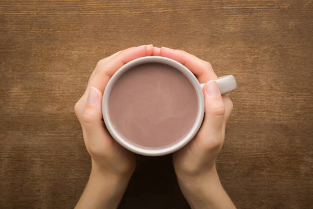 Young adult woman hands holding cup of cocoa on dark brown wooden table background. Closeup. Point of view shot. Top down view. stock photo