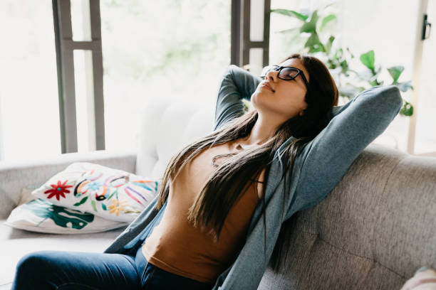 Young adult woman relaxing at home, sitting on the sofa Young adult woman relaxing at home, sitting on the sofa. Hispanic ethnicity. relief emotion stock pictures, royalty-free photos & images