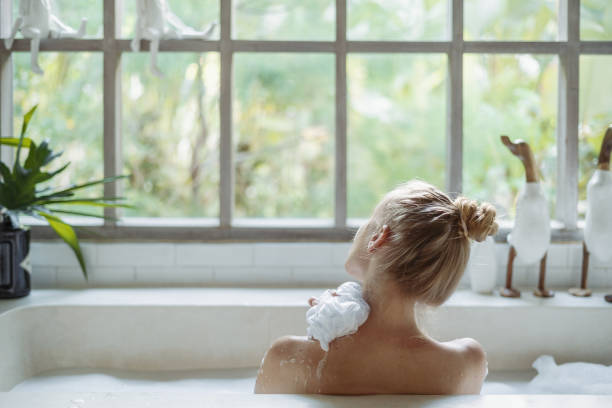 junge erwachsene frau nimmt bad halten schwamm in der hand, gewaschene schulter - körperpflege stock-fotos und bilder