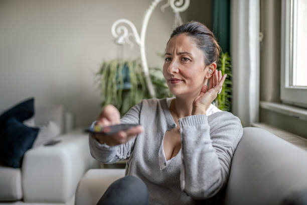 молодая взрослая женщина со слуховой помощью смотрит телевизор - hearing aids стоковые фото и изображения