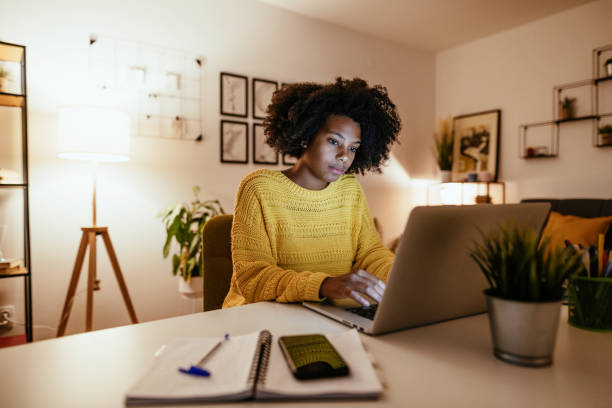 joven empresaria afroamericana en el escritorio, trabajando hasta tarde - woman on computer fotografías e imágenes de stock