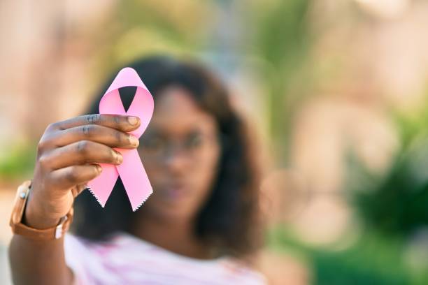 молодая афроамериканка с серьезным выражением лица держит в руках розовую ленту рака молочной железы в городе. - breast cancer стоковые фото и изображения