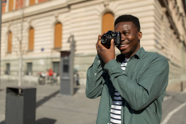 young african american male photographer taking photos around the city - fotograaf stockfoto's en -beelden