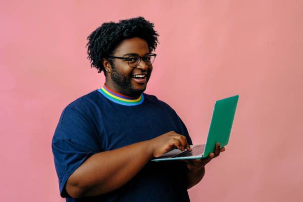 young african american man posing with laptop in the studio over pink background stock photo