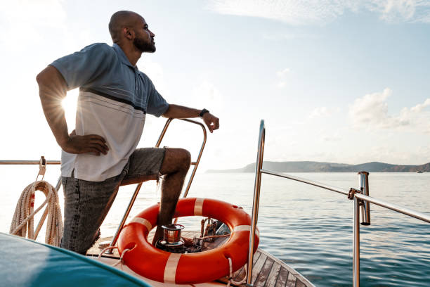 Young african american man relaxing on a sailboat in open sea at sunset stock photo