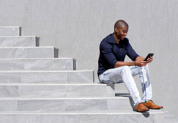 young african american man sitting on steps using tablet stock photo