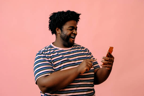 young african american man with a phone posing in the studio over pink background stock photo