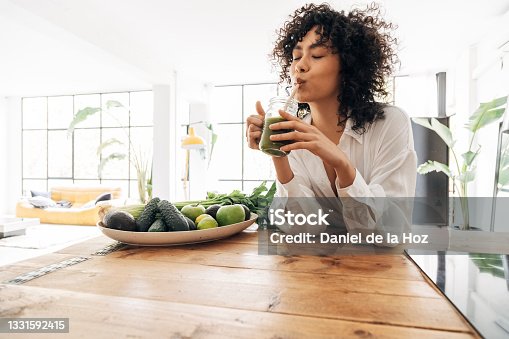 istock Young african american woman drinking green juice with reusable bamboo straw in loft apartment. Copy space 1331592415