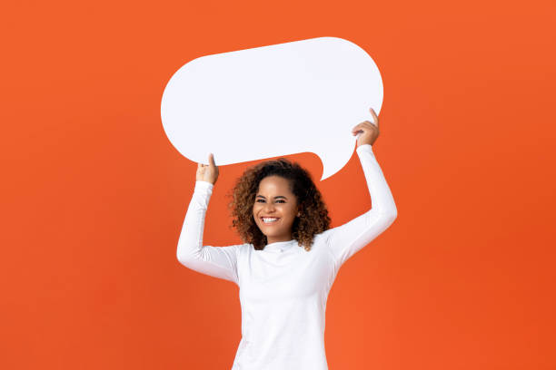 Young African American woman holding empty speech bubble Happy young African American woman in plain white long sleeve t-shirt holding empty speech bubble isolated on orange  background speech bubble photos stock pictures, royalty-free photos & images
