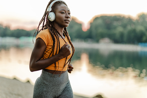 African American woman doing sport by the river and listening music with headphones
