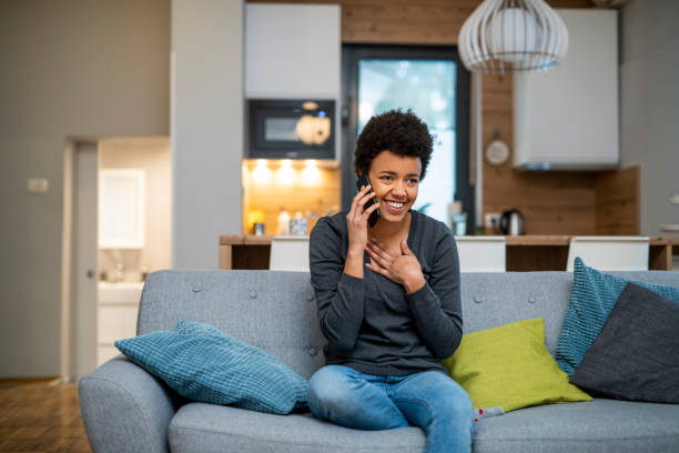 Young African American woman making a phone call and sitting on the sofa Young African American woman making a phone call and sitting on the sofa relief emotion stock pictures, royalty-free photos & images