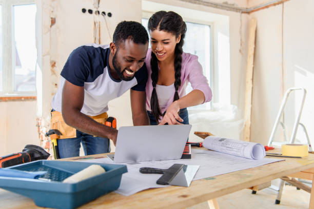 young african american woman pointing at laptop screen to boyfriend during renovation of home young african american woman pointing at laptop screen to boyfriend during renovation of home home improvement stock pictures, royalty-free photos & images