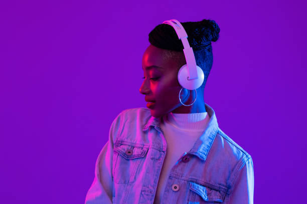 Young African American woman wearing headphones listening to music in futuristic purple cyberpunk neon light background stock photo
