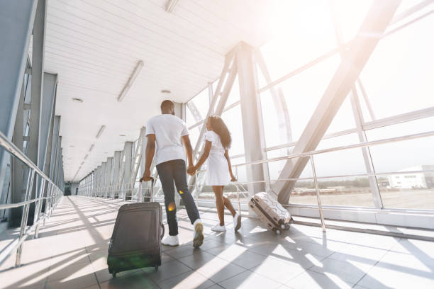 Young african couple walking with luggage at airport building Going to flight. Young african couple walking with luggage at airport building, empty space airport terminal photos stock pictures, royalty-free photos & images