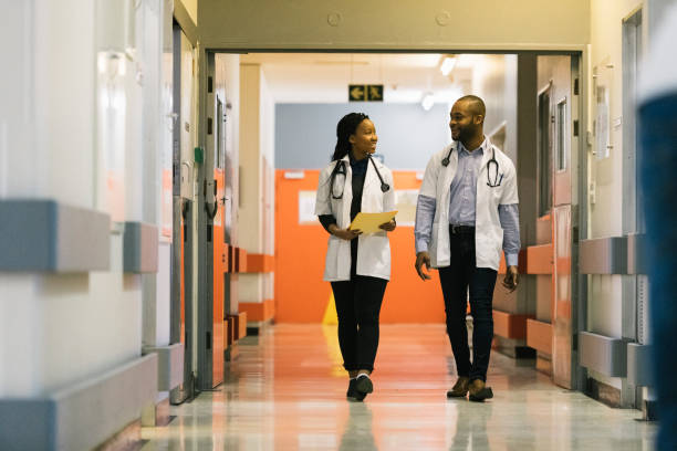 Young African doctors walking down hospital corridor talking stock photo