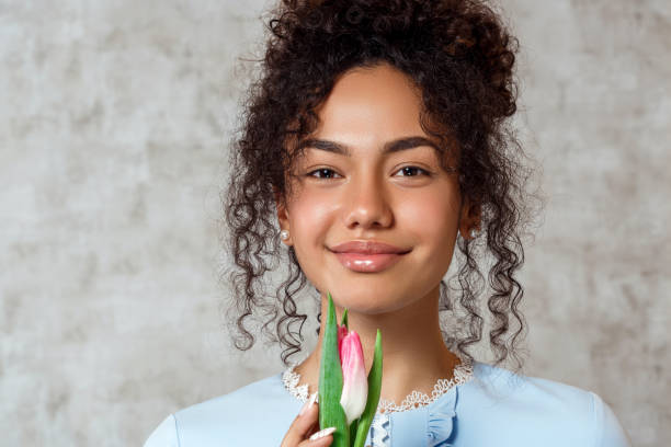 Young African girl in a blue dress with a Tulip on a gray background. The concept of women's day and spring stock photo