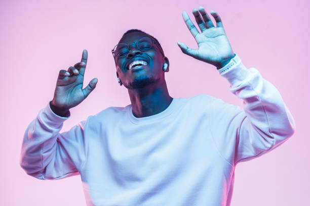 Young african man listening to music with wireless earphones and dancing isolated on pink background  rapper stock pictures, royalty-free photos & images