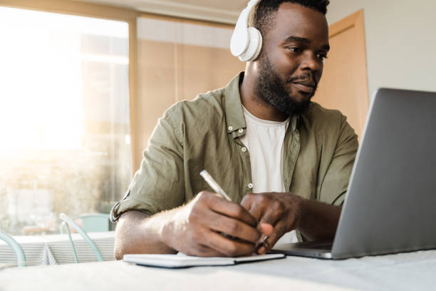 Young african man using computer laptop while wearing headphones at bar restaurant - Conference video call lifestyle technology concept - Focus on face stock photo
