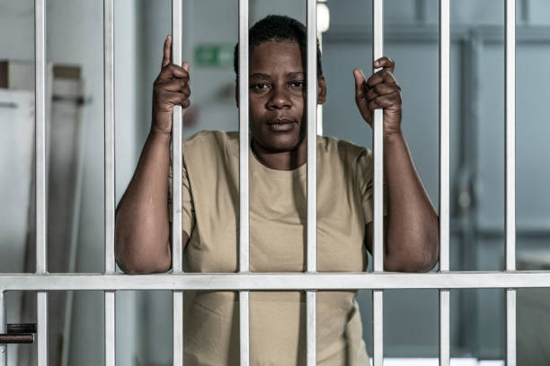 Young afro woman looking  serious and desperate   behind bars which may be prison bars or those of a security gate stock photo