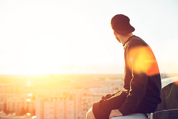 Young and brave man sitting on edge of the roof stock photo