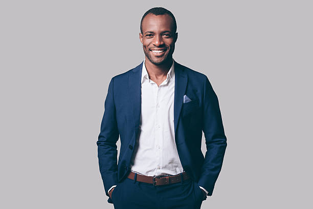 Young and handsome. Handsome young African man in smart casual jacket holding hands in pockets and smiling while standing against grey background business suit stock pictures, royalty-free photos & images