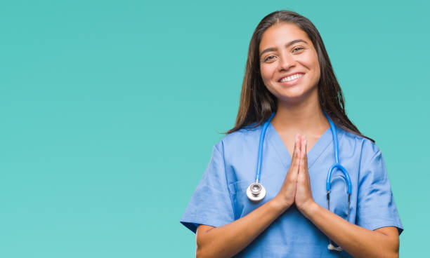 Young arab doctor surgeon woman over isolated background praying with hands together asking for forgiveness smiling confident.  prayer request stock pictures, royalty-free photos & images