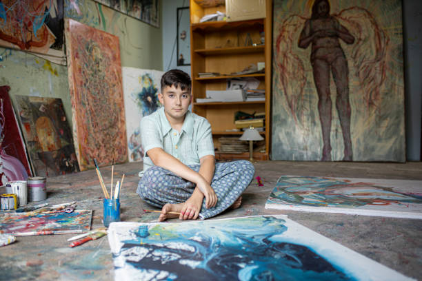 Seorang seniman muda melukis kanvas di lantai studio foto stok