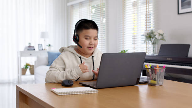 Young asia boy student wear headset headphone with computer laptop videocall talk present online e-learning class study with teacher, social distance learn language at home, homeschooling concept. stock photo