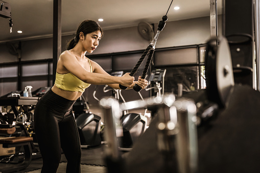 Young Asia lady exercise doing exercise-machine Cable Crossover fat burning workout in fitness class. Athlete with six pack, Sportswoman recreational activity, functional training, healthy lifestyle.